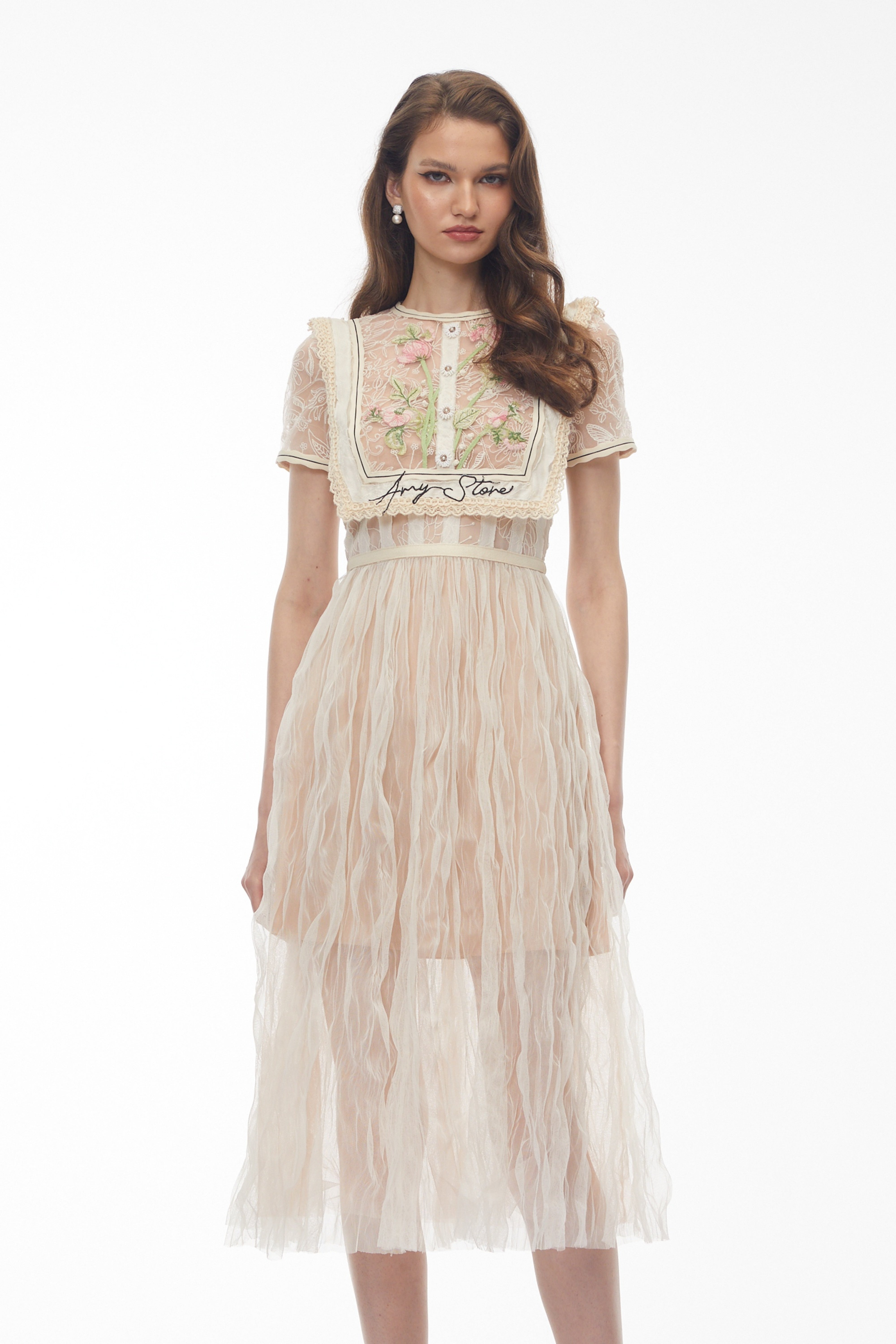 فستان ميدي باللون البيج من الدانتيل، مزين بتطريزات زهرية وتفاصيل على شكل صدرية