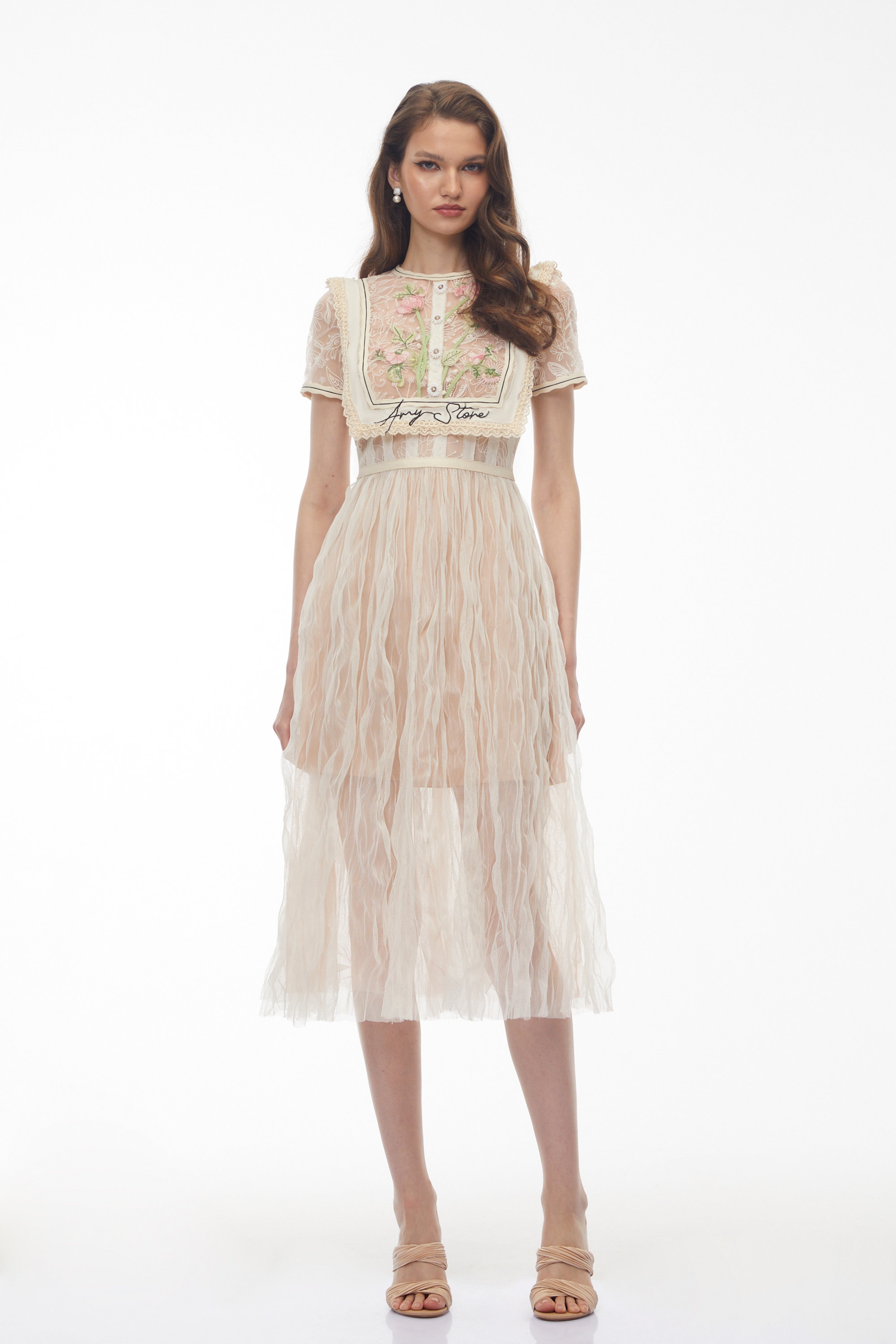 فستان ميدي باللون البيج من الدانتيل، مزين بتطريزات زهرية وتفاصيل على شكل صدرية