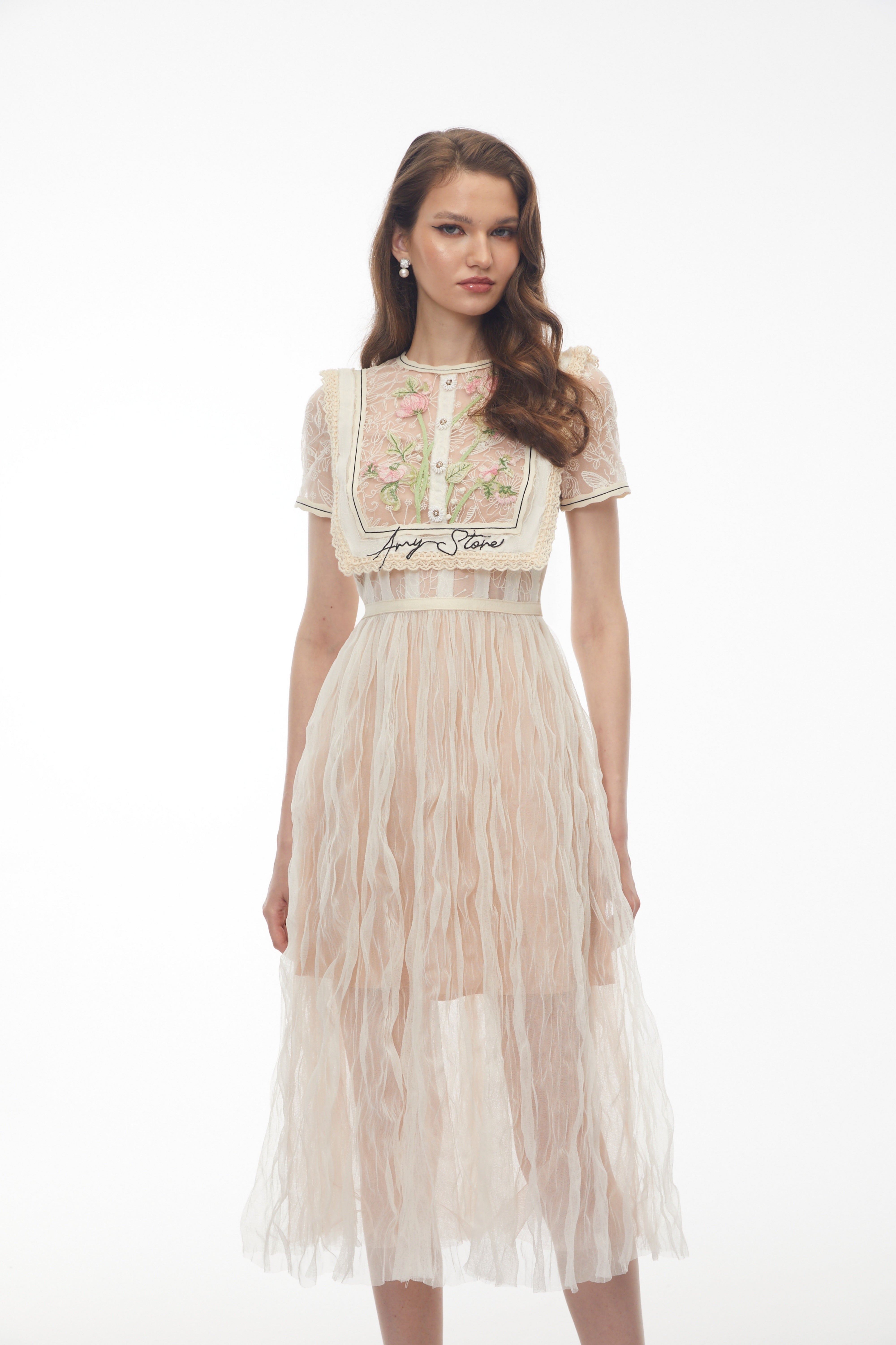 فستان ميدي باللون البيج من الدانتيل، مزين بتطريزات زهرية وتفاصيل على شكل صدرية